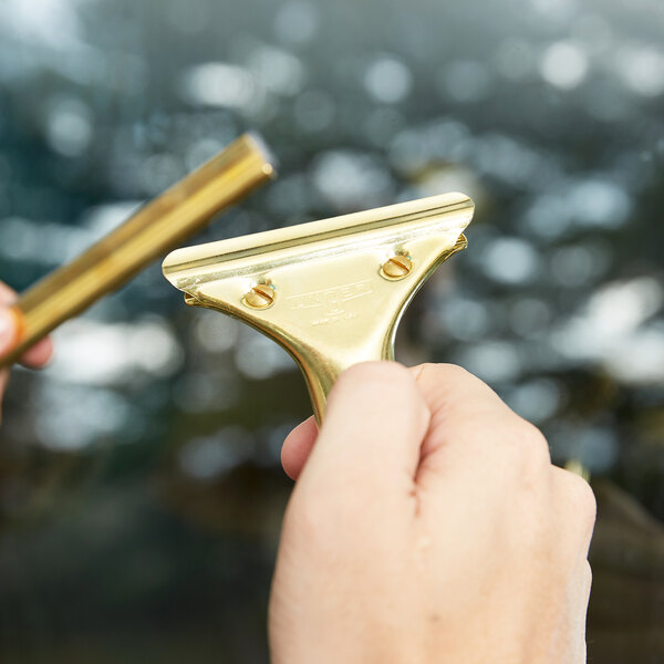 A hand holding a Unger GoldenClip brass squeegee handle.