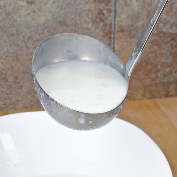A Vollrath stainless steel ladle pouring white liquid into a bowl.