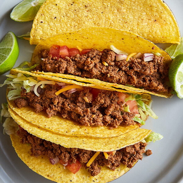 A plate with three tacos filled with Vanee beef taco filling, lettuce, and other vegetables.