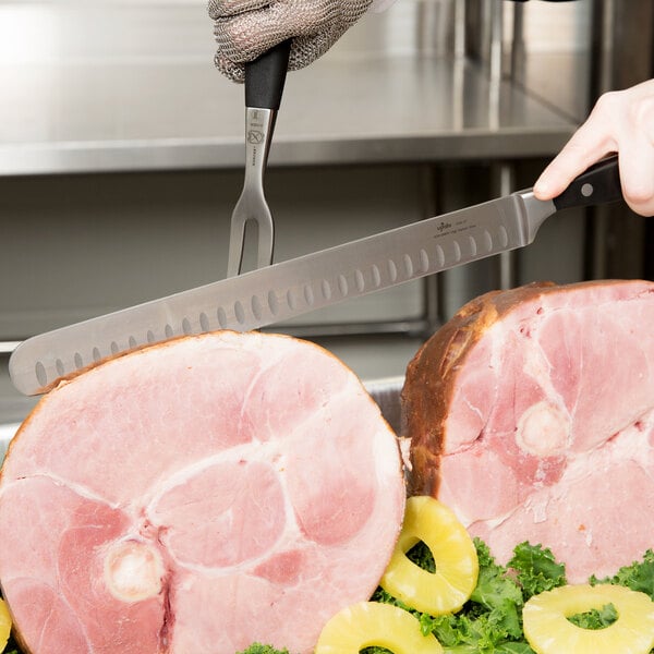 A person using a Winco Granton Edge Carving Knife to cut a ham.