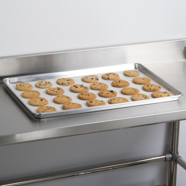 An Advance Tabco aluminum sheet pan with cookies on it on a metal surface.