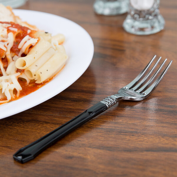 A WNA Comet Reflections Duet heavy weight plastic fork with black handle on a plate of pasta.