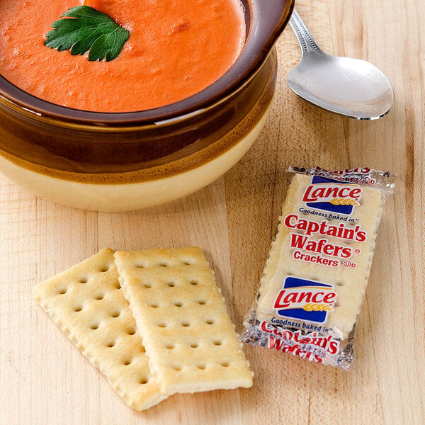 A bowl of tomato soup next to Lance Captain's Wafer crackers and a spoon.