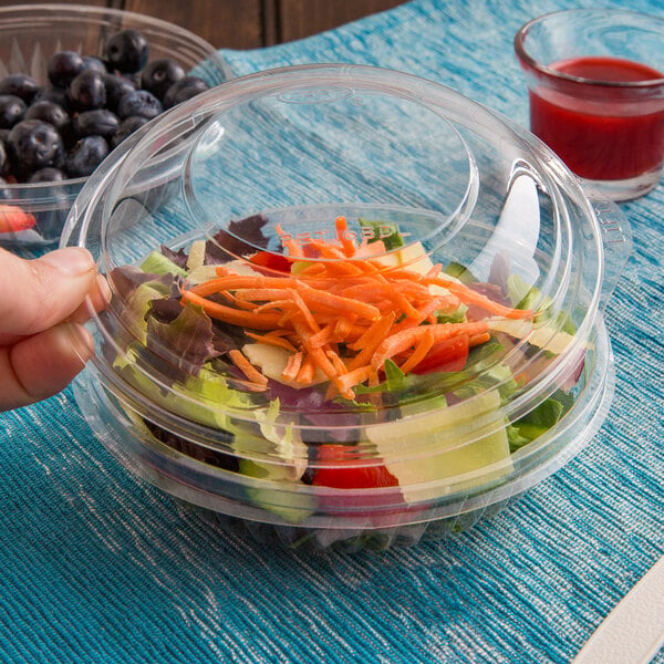 A hand holding a Dart plastic container of salad with a dome lid.