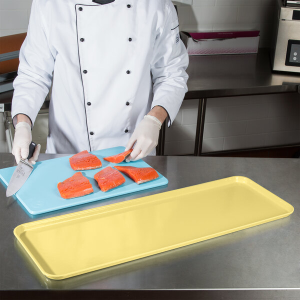 A person cutting salmon on a Cambro yellow market tray.