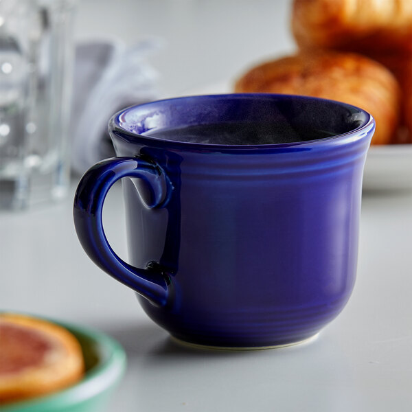 A blue Tuxton round china cup with liquid in it on a table.