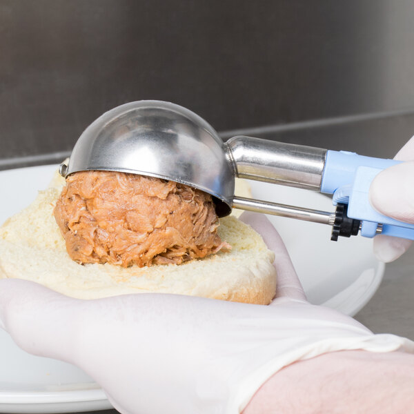 A person using a Vollrath metal scoop to put food on a sandwich.