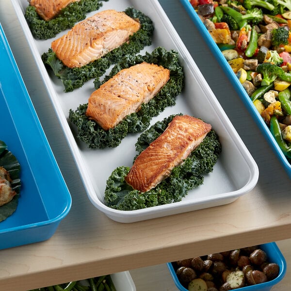 A white fiberglass market pan filled with food, including salmon and kale, on a table.