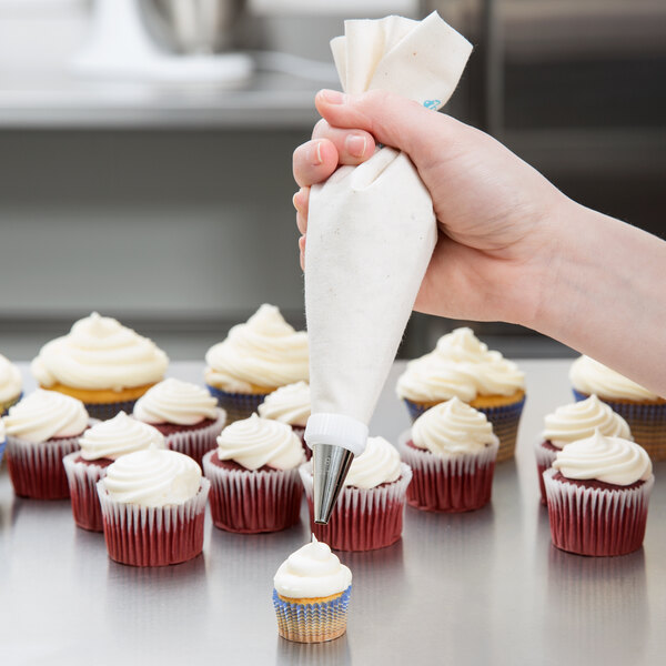 A person using an Ateco plastic coated canvas pastry bag to frost a cupcake.