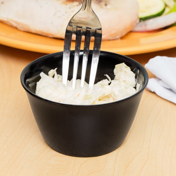 A fork in a black Carlisle bouillon cup filled with coleslaw.