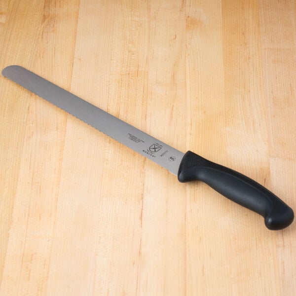 A Mercer Culinary Millennia 11" Serrated Edge Slicer Knife with a black handle on a wooden table.