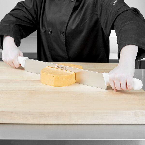 A person using a Dexter-Russell cheese knife to cut cheese on a wooden cutting board.