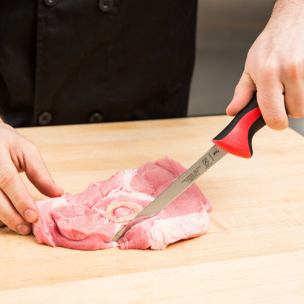A person using a Mercer Culinary Millennia Colors narrow boning knife to cut meat on a cutting board.