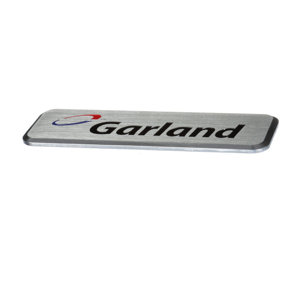 A silver rectangular metal badge with the word "Garland" in black text.