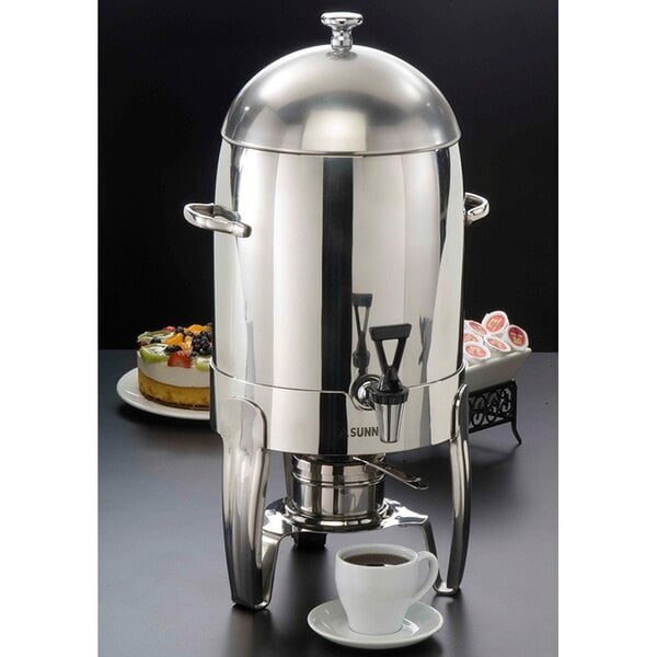 An American Metalcraft stainless steel coffee chafer urn with a cup of coffee and a saucer.