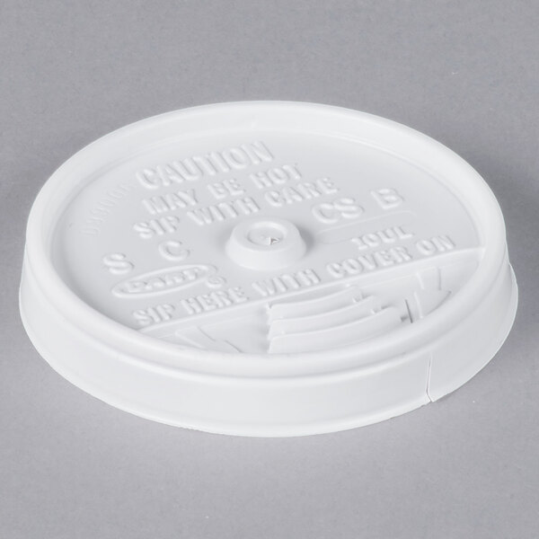A Dart white plastic sip thru lid on a table with text on it.
