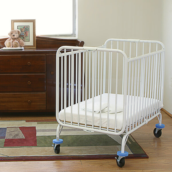An L.A. Baby metal folding crib with a mattress in a room.
