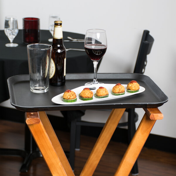 A black Cambro non-skid serving tray with food and wine glasses on a table.