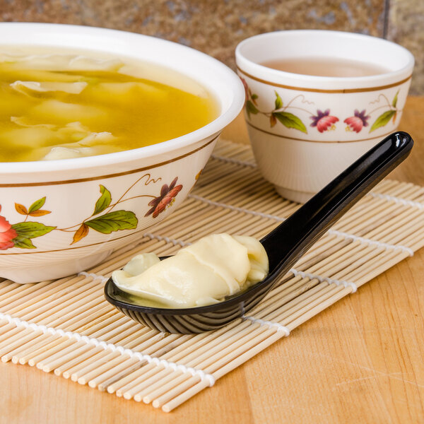 A bowl of soup with a black melamine Chinese soup spoon on a counter.