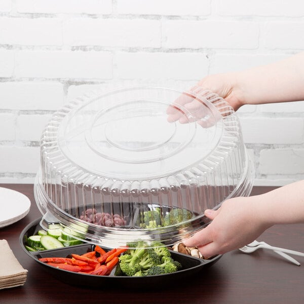 A person holding a Fineline clear plastic lid over a tray of vegetables.