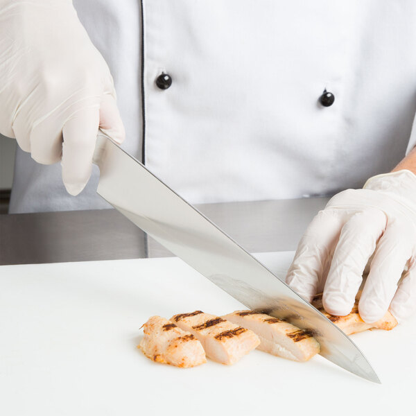 A person using a Mercer Culinary Sujihiki knife to cut meat on a white cutting board.