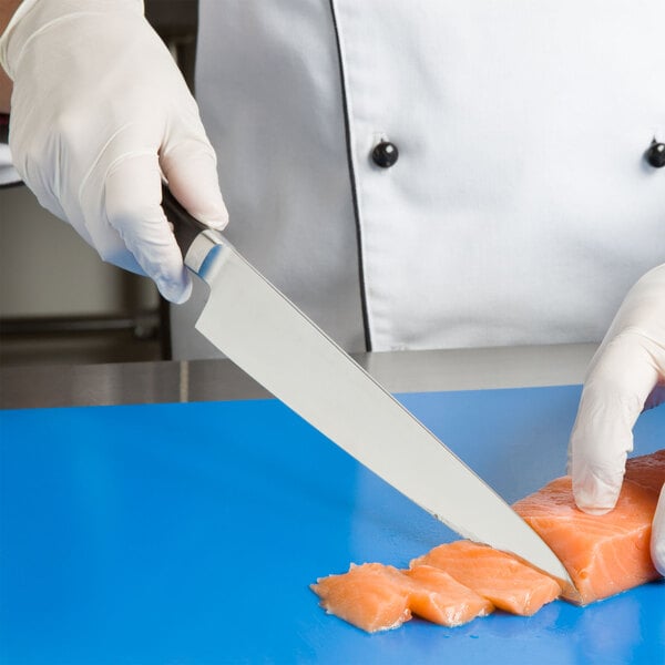 Chef in white disposable gloves using a Japanese knife to cut raw fish