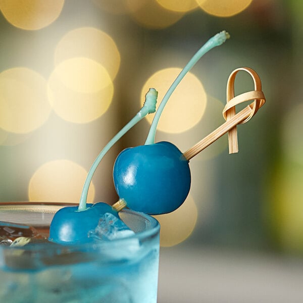A blue cherry on a stick in a glass of blue liquid.
