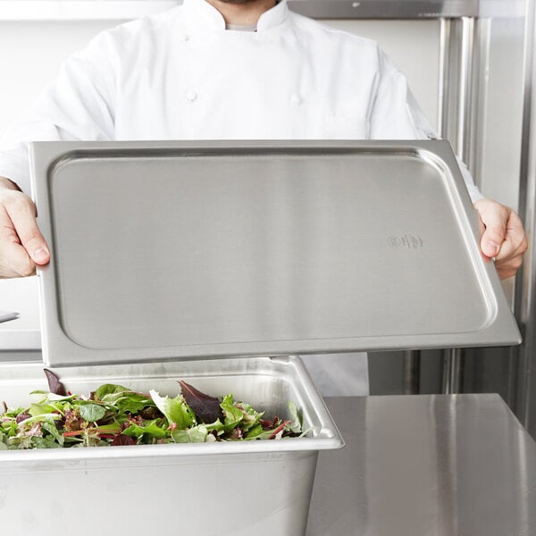 A chef using a Vollrath stainless steel pan cover to seal a container of salad.