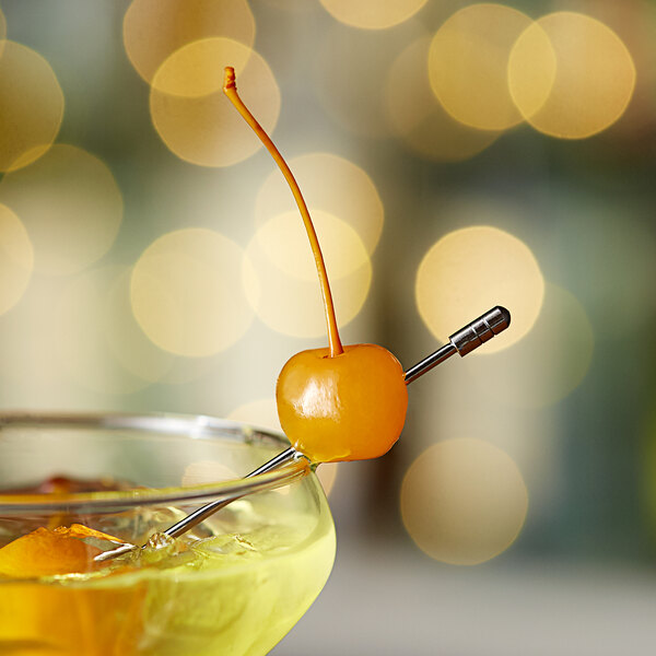 A glass of orange juice on a table in a cocktail bar with a yellow maraschino cherry on the rim.