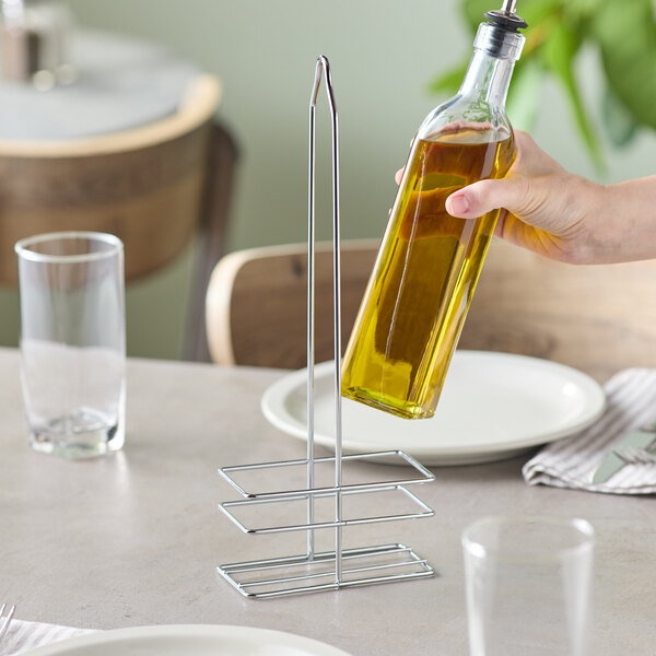 A hand pouring olive oil into a metal rack on a table in a home kitchen.