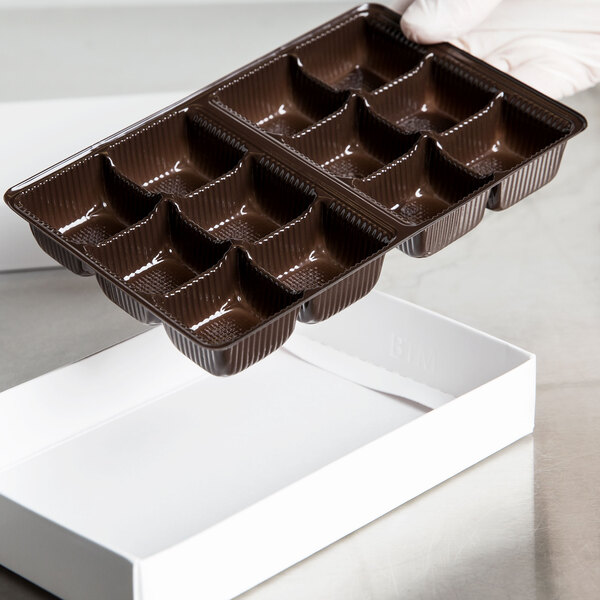 A hand holding a brown plastic candy tray filled with chocolate.