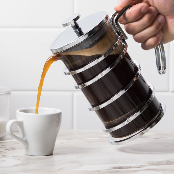 A hand pouring coffee into a Libbey stainless steel French press.