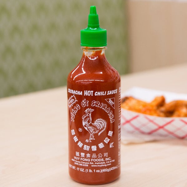 A bottle of Huy Fong Sriracha Hot Chili Sauce on a table.