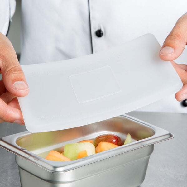 A chef using a white Flexsil high-heat silicone lid on a plastic container of fruit.