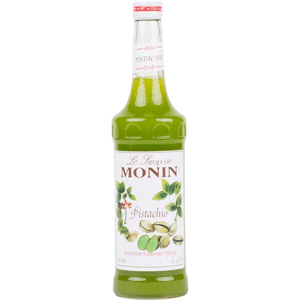 A bottle of Monin pistachio flavoring syrup with a white label filled with green liquid.