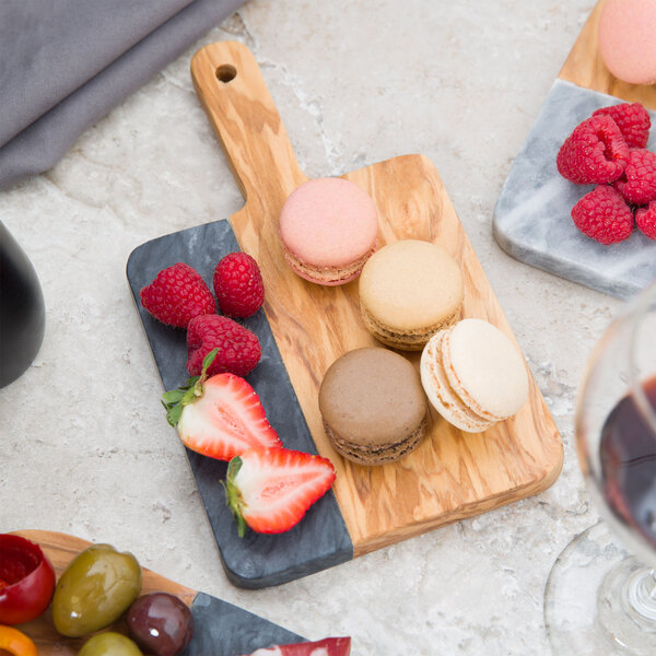 An American Metalcraft olive wood and black marble serving board with fruit and macaroons on a table.