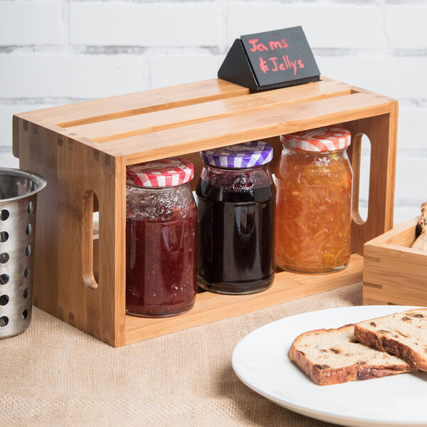 An American Metalcraft bamboo wood crate with jars of jam and a plate of bread on a table.