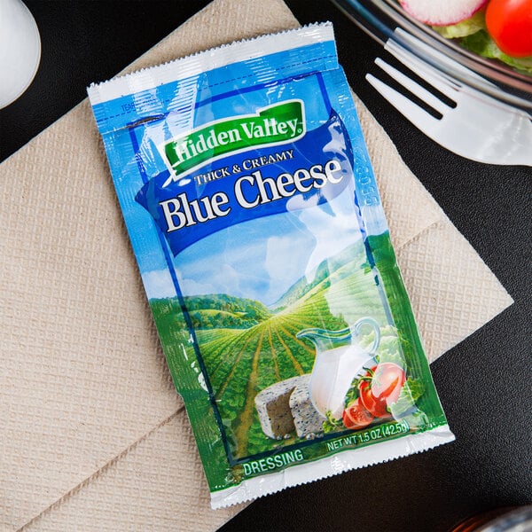 A Hidden Valley blue cheese dressing packet on a napkin next to a bowl of salad.