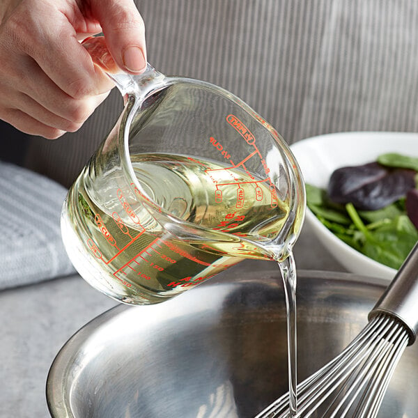 A person pouring 100% organic soybean oil from a measuring cup into a bowl.