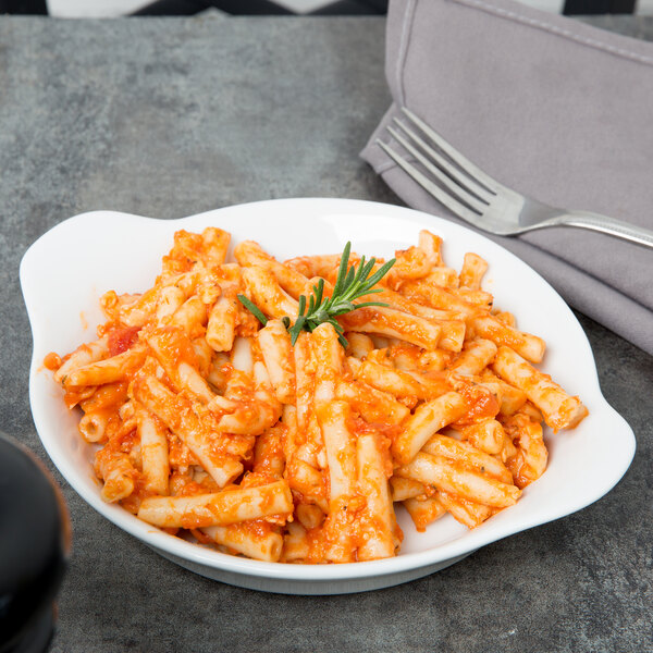 A Libbey aluma white porcelain handled dish filled with pasta with tomato sauce and a fork.