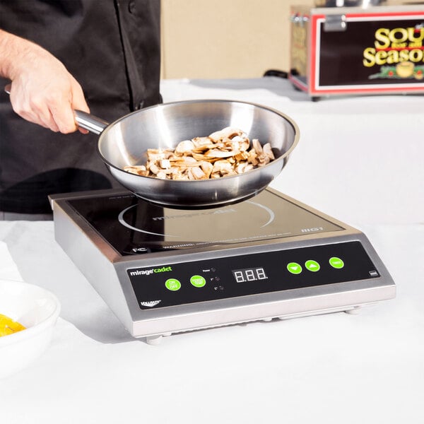 A chef using a Vollrath countertop induction range to cook mushrooms in a pan.