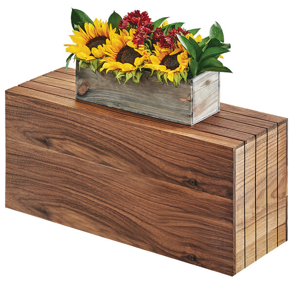 A wooden rectangular riser with sunflowers and red flowers on top of it.