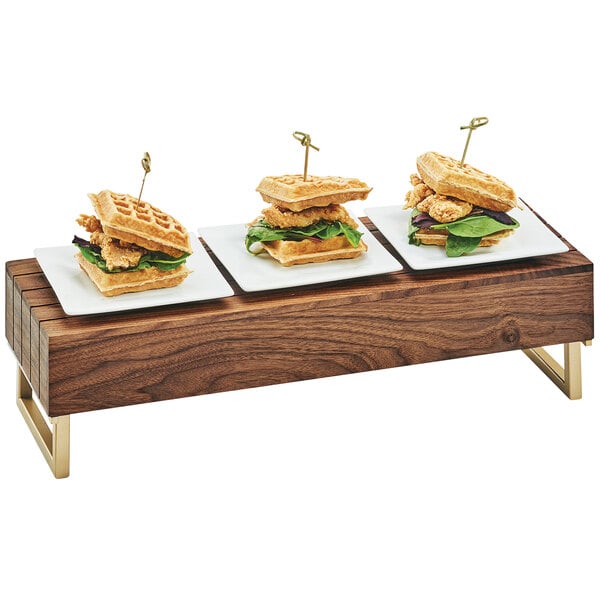 A row of waffle sandwiches on a walnut wood and brass display riser.
