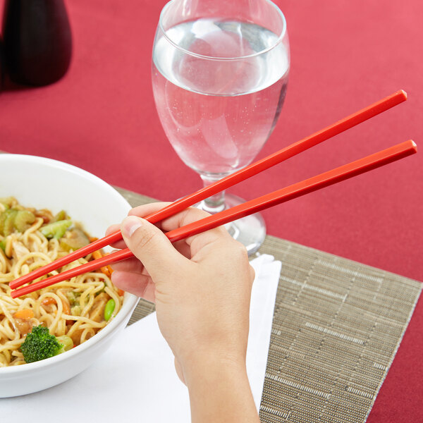 A hand holding Town Red Plastic Chopsticks over a bowl of noodles.