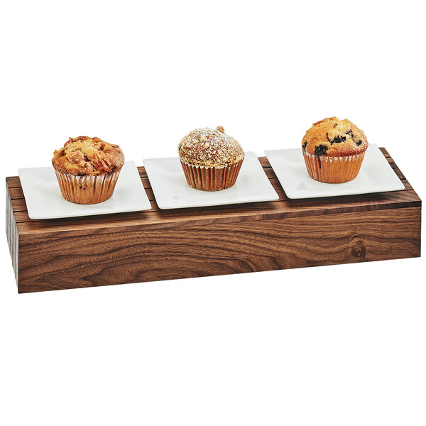 A walnut rectangular riser with three muffins on a wood tray.