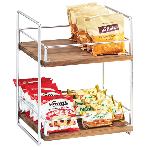 A Cal-Mil two tier wood and chrome merchandiser shelf with snacks on it.