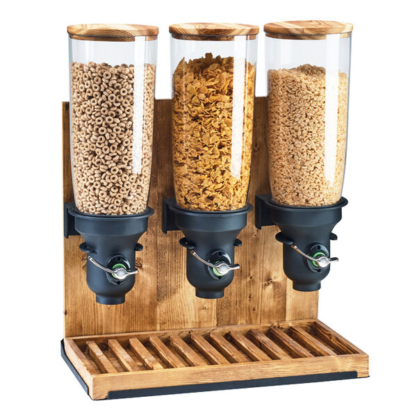 A Cal-Mil Madera triple cereal dispenser with glass jars of cereal on a wooden stand.