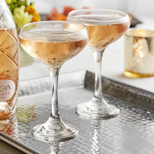 A pair of Acopa coupe cocktail glasses on a tray with a bottle of champagne.