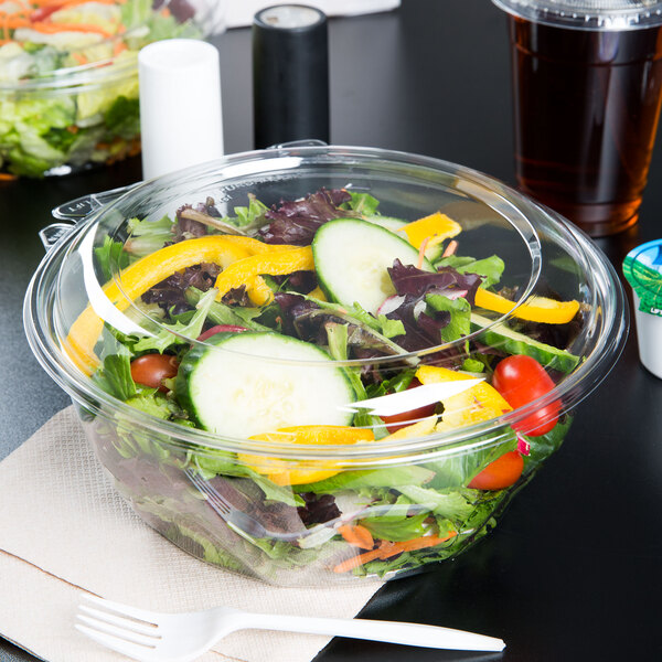 A salad in a Dart plastic bowl with a dome lid on a table.