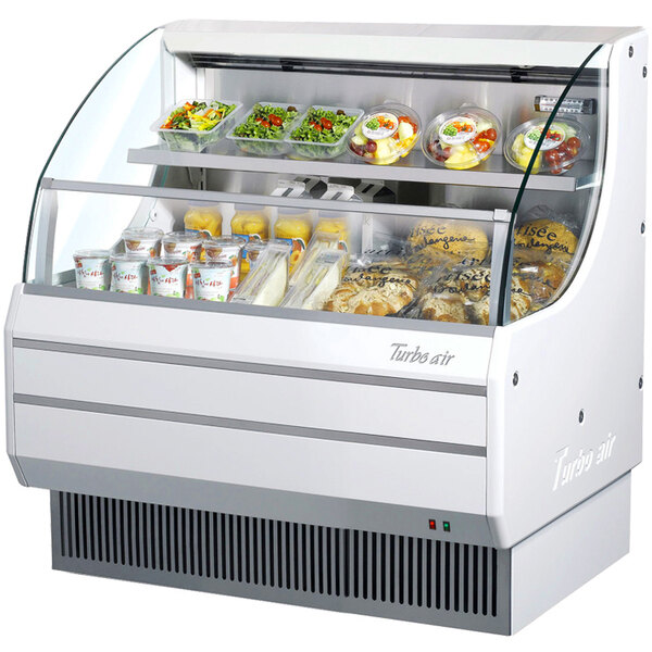 A white Turbo Air low profile horizontal air curtain display case on a counter with food inside.